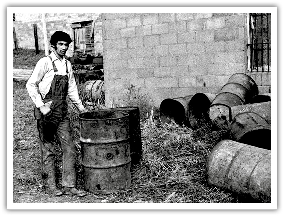 A photo from the Omaha World-Herald's report on the murder of Agatha White Buffalo. A man stands behind the back of the abandoned tannery among discarded oil barrels. White Buffalo's body was found inside one of the barrels. 