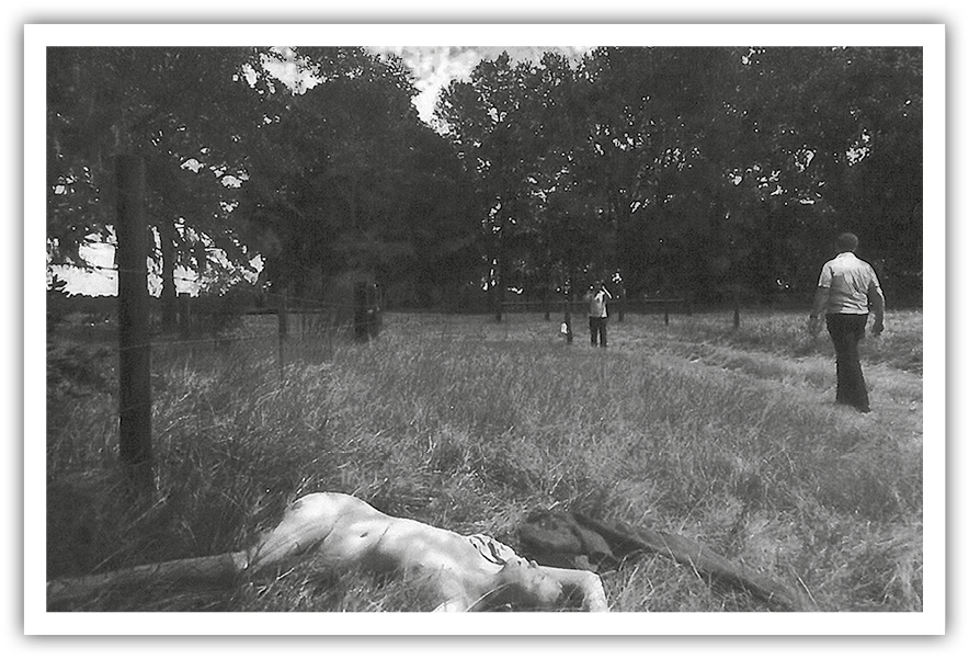 A photo of the Patricia Mount crime scene. A nude body is seen in an empty field with two men standing by.